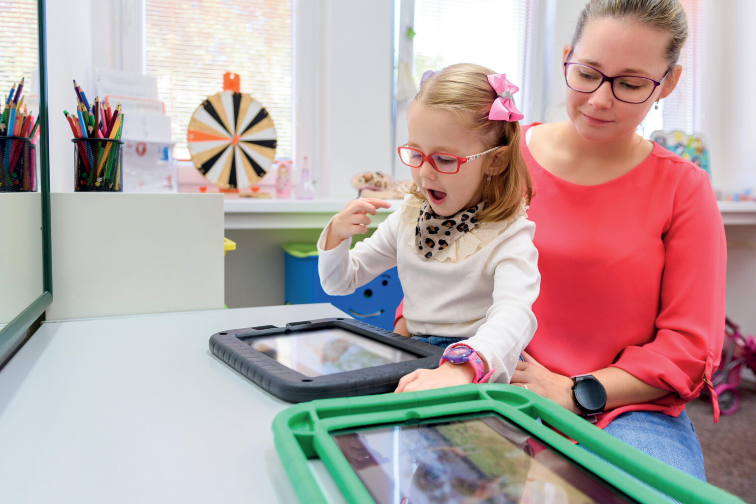 une adulte aide une petite fille devant une tablette interactive