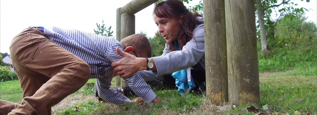une femme aide un enfant dans un jeu exterieur