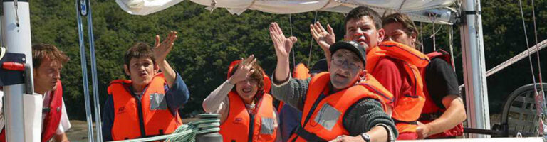 un groupe d'adulte avec des bouées de sauvetage sur un bateau salue de la main