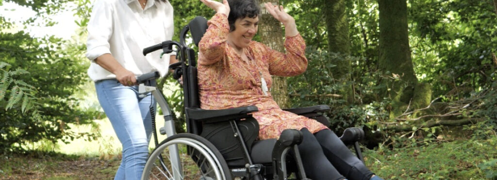 une femme en fauteuil roulant sourit et leve les bras